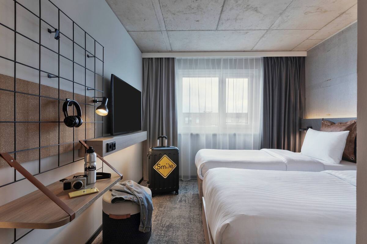 A hotel room with two beds, a desk with a computer, a television, and a window with curtains.