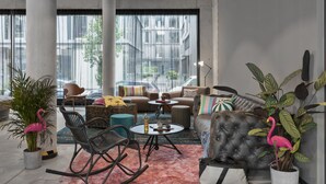 A modern living room with a sofa, chairs, a coffee table, and potted plants. - Moxy Hamburg Altona (Hamburg)