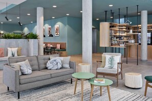 A modern lounge area with a grey sofa, round wooden tables, and a bar area with shelves of bottles. - Residence Inn by Marriott Hamburg Altona (Hamburg)