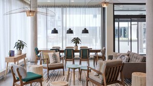 A modern lounge area with a mix of seating options, including sofas, chairs, and a dining table. There are potted plants and a large window providing natural light. - Residence Inn by Marriott Hamburg Altona (Hamburg)