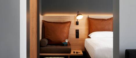 Habitación de hotel pequeña con cama, mesita de noche, zona de estar y maleta con un par de zapatos.