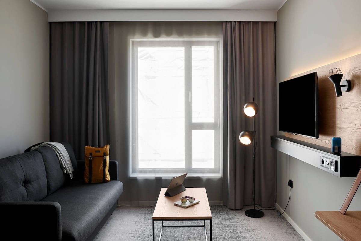 Una sala de estar moderna con un sofá, una mesa de centro con una computadora portátil, un televisor montado en la pared y una lámpara de pie.