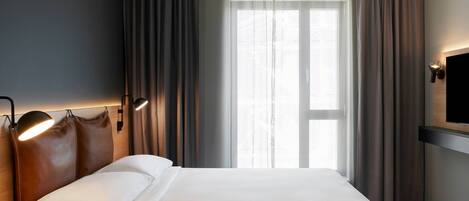 Habitación de hotel con una cama grande, televisor de pantalla plana en la pared y una ventana con cortinas.