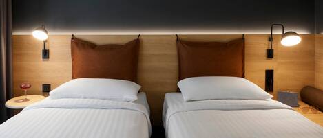 A hotel room with two beds, a bedside table with a glass of red wine, and a lamp.
