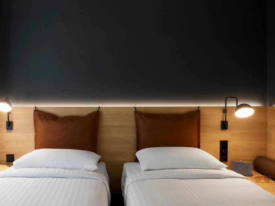 A hotel room with two beds, a bedside table with a glass of red wine, and a lamp.