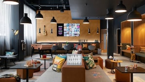 A modern lounge area with seating, tables, and a large screen displaying content. - Moxy Milton Keynes (Milton Keynes)