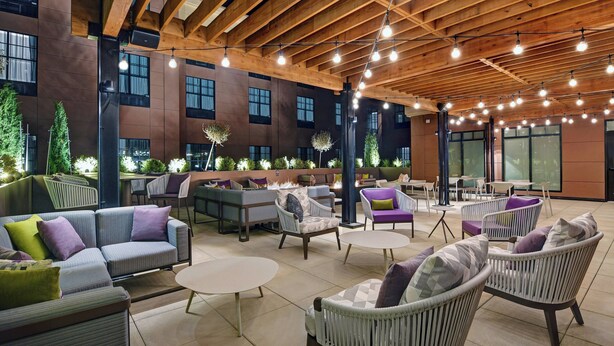 An outdoor seating area with modern furniture, a wooden ceiling, and large windows. - Courtyard by Marriott Manhattan Aggieville (Manhattan)