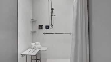 A modern shower area with a handheld showerhead, a towel rack, and a small table with towels.