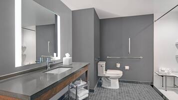 A modern bathroom with a large mirror, dual sinks, a toilet, and a shower area.