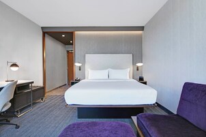 Una habitación de hotel moderna con una cama grande, un escritorio, una silla y un sofá morado.