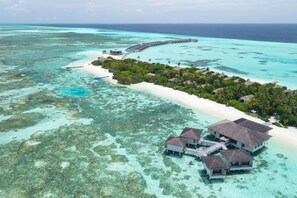Vista aérea de un resort con bungalows sobre el agua, una playa y un arrecife de coral.