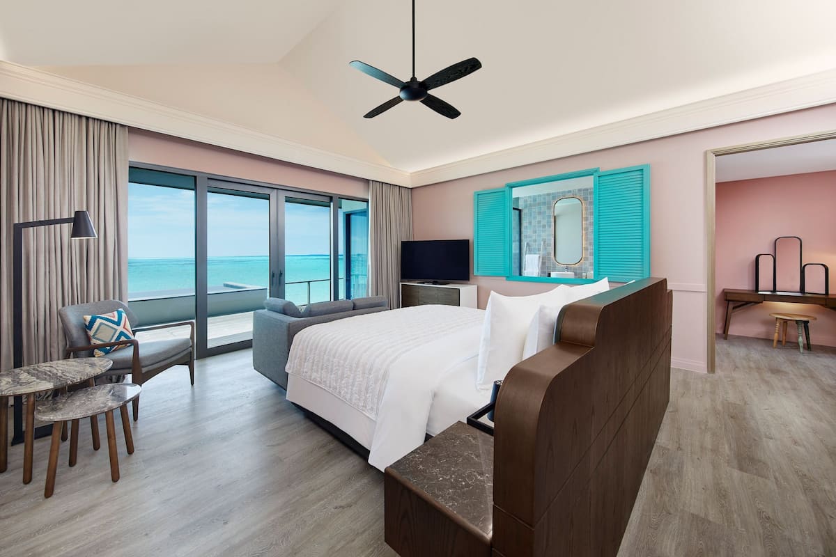 Ein modernes Hotelzimmer mit einem großen Bett, einem Schreibtisch, einem Sessel, einem Fernseher und Blick aufs Meer.