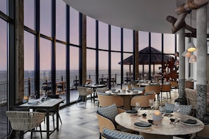 Un vaste espace extérieur aménagé pour les repas, doté de hauts plafonds et de grandes fenêtres offrant une vue panoramique.