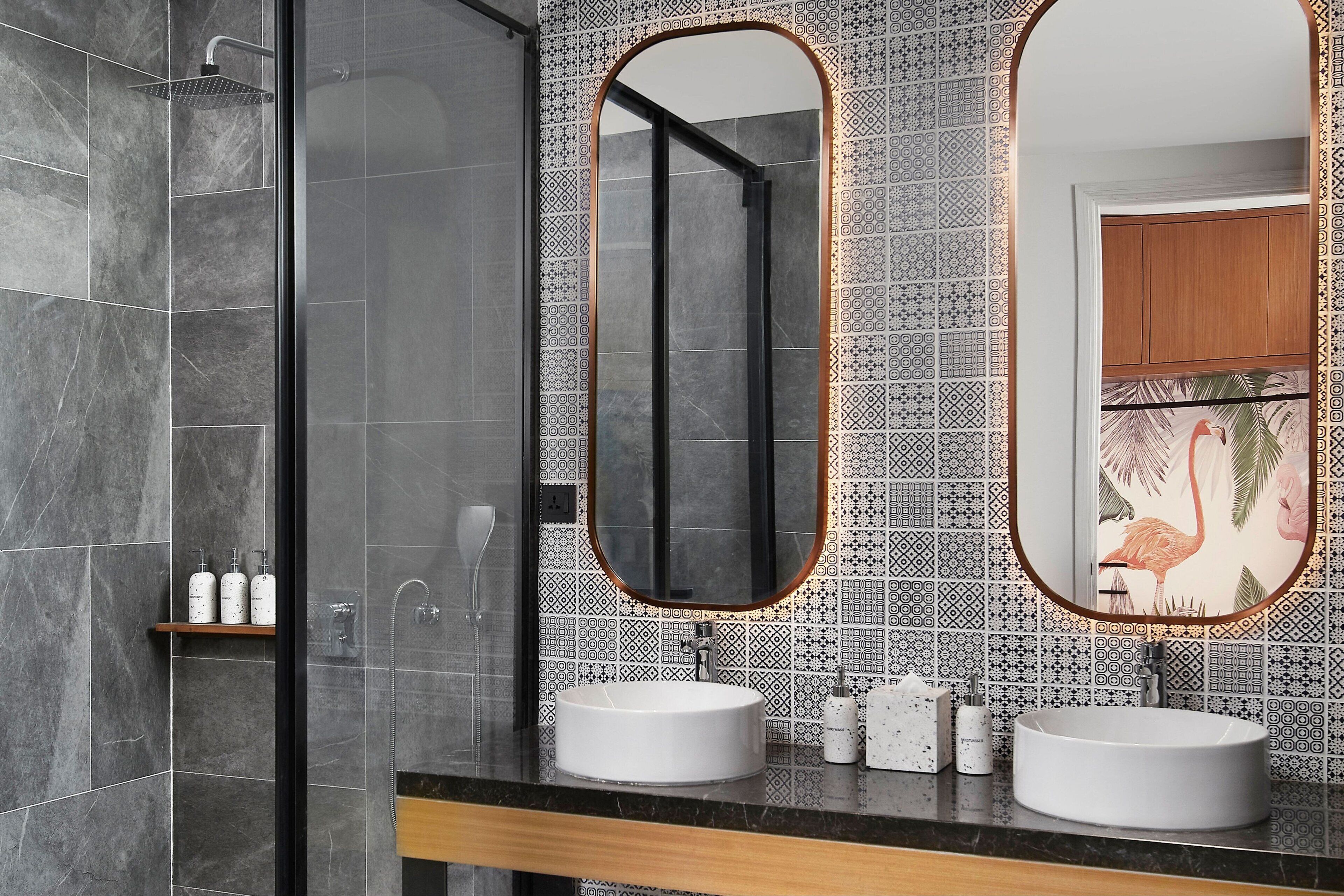 Ein modernes Badezimmer mit zwei Waschbecken, einer Dusche und einem großen Spiegel mit dekorativem Rahmen.