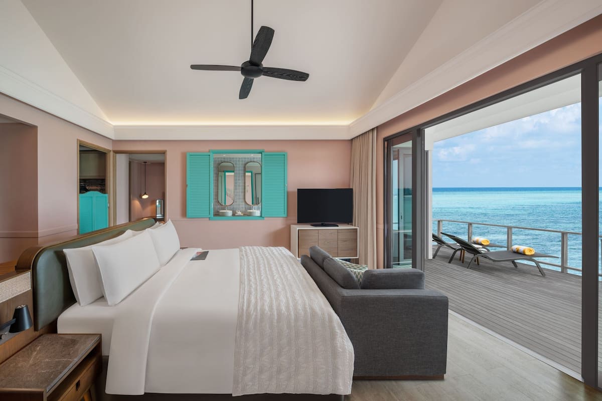 Ein Hotelzimmer mit Bett, Fernseher, Sofa und einem Balkon mit Meerblick.