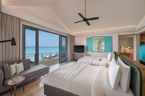 A hotel room with a large bed, a sofa, a TV, and a balcony with a view of the ocean.