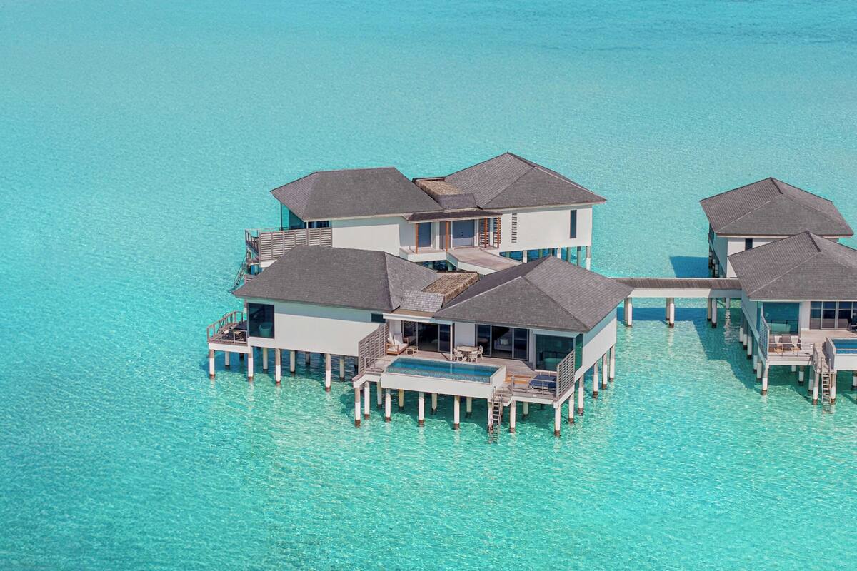 Eine Luftaufnahme von Bungalows über dem Wasser mit mehreren Ebenen, verbunden durch Wege, umgeben von klarem türkisblauem Wasser.