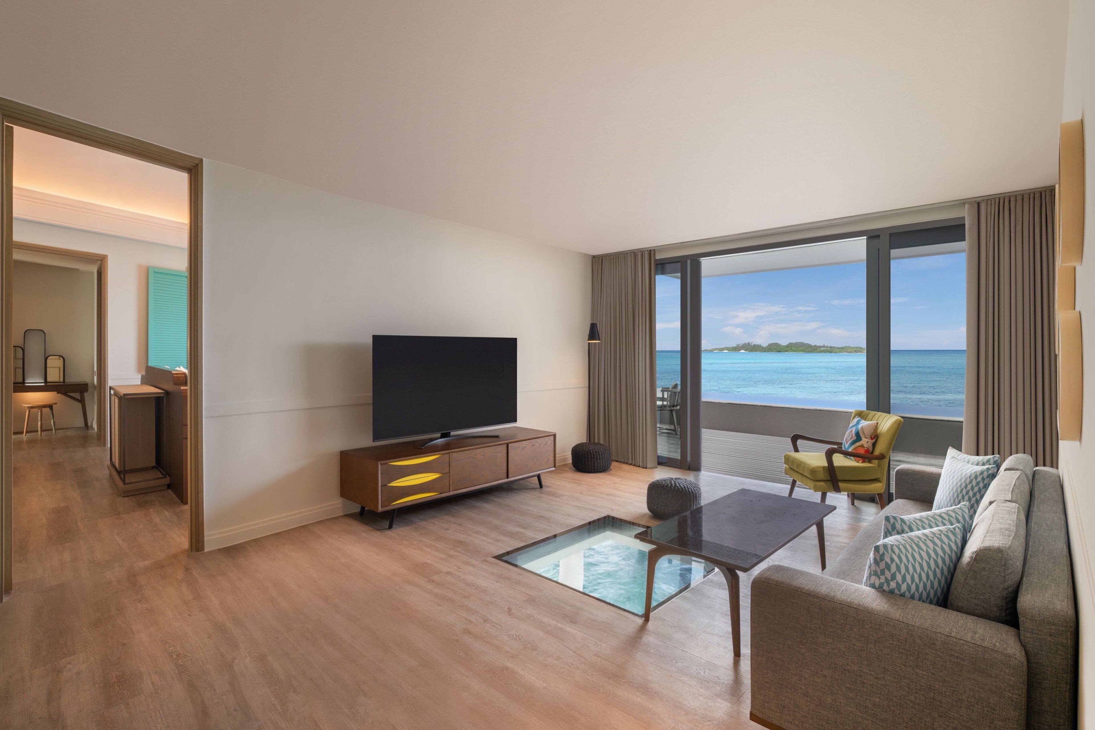 A modern hotel room with a large television, a sofa, a coffee table, and a view of the ocean.