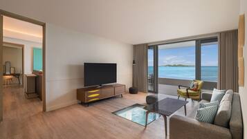 A modern hotel room with a large television, a sofa, a coffee table, and a view of the ocean.