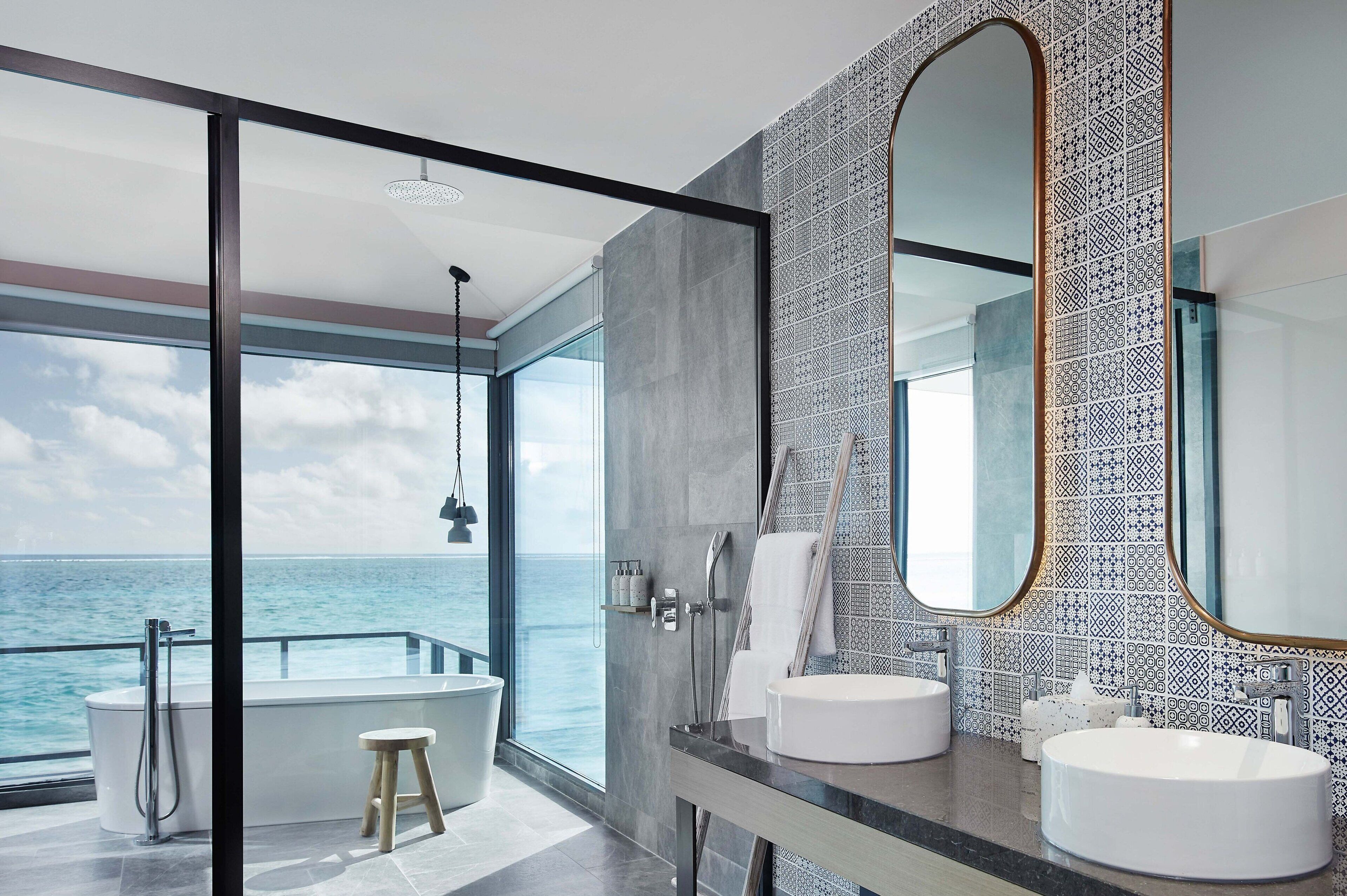 Une salle de bain moderne avec deux lavabos, un grand miroir et une vue sur l’océan.