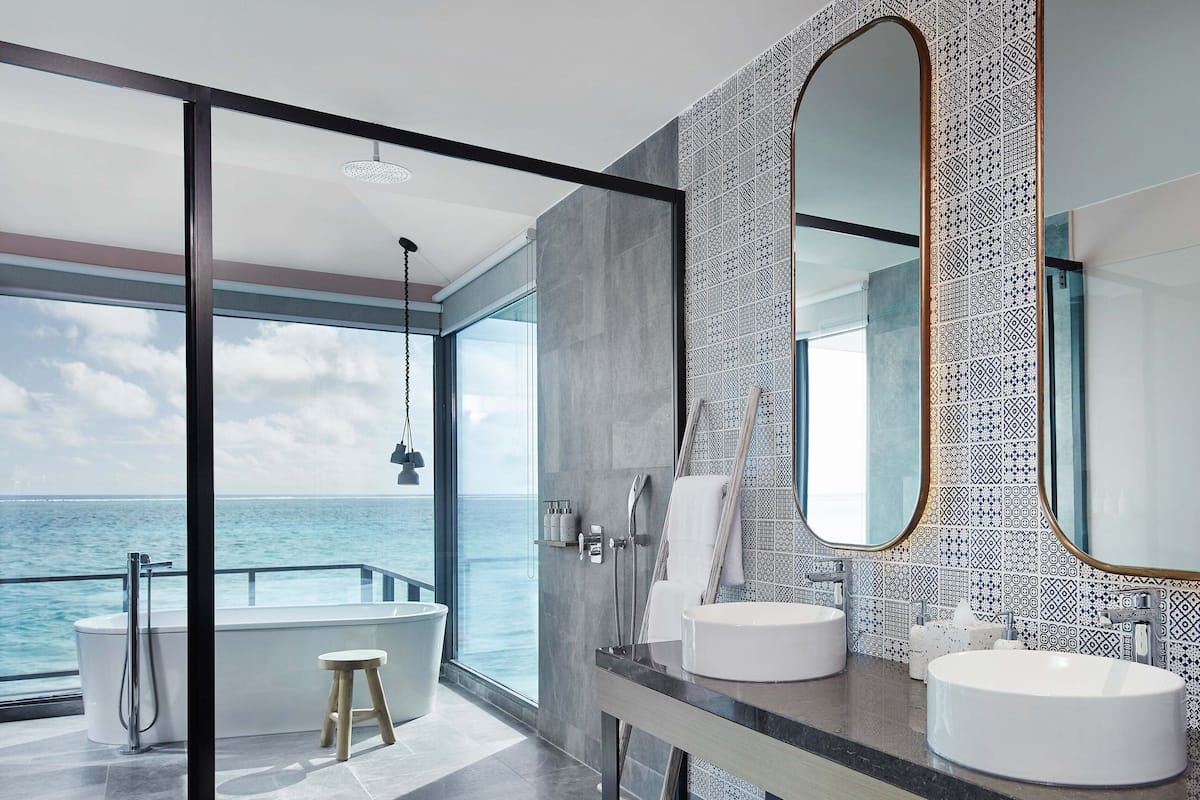 Un baño moderno con dos lavabos, un espejo grande y vista al océano.