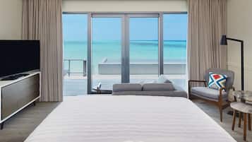 A hotel room with a large bed, a TV, a chair, and a view of the ocean through large windows.
