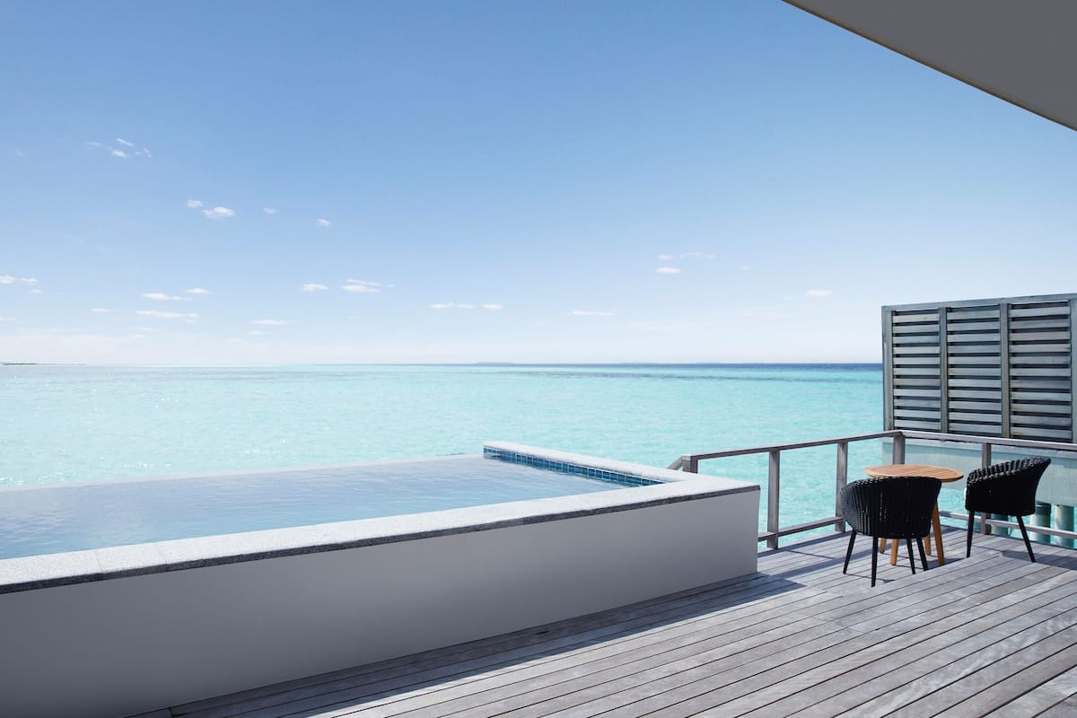 Terraza con piscina y dos sillas, con vista al mar azul y transparente.