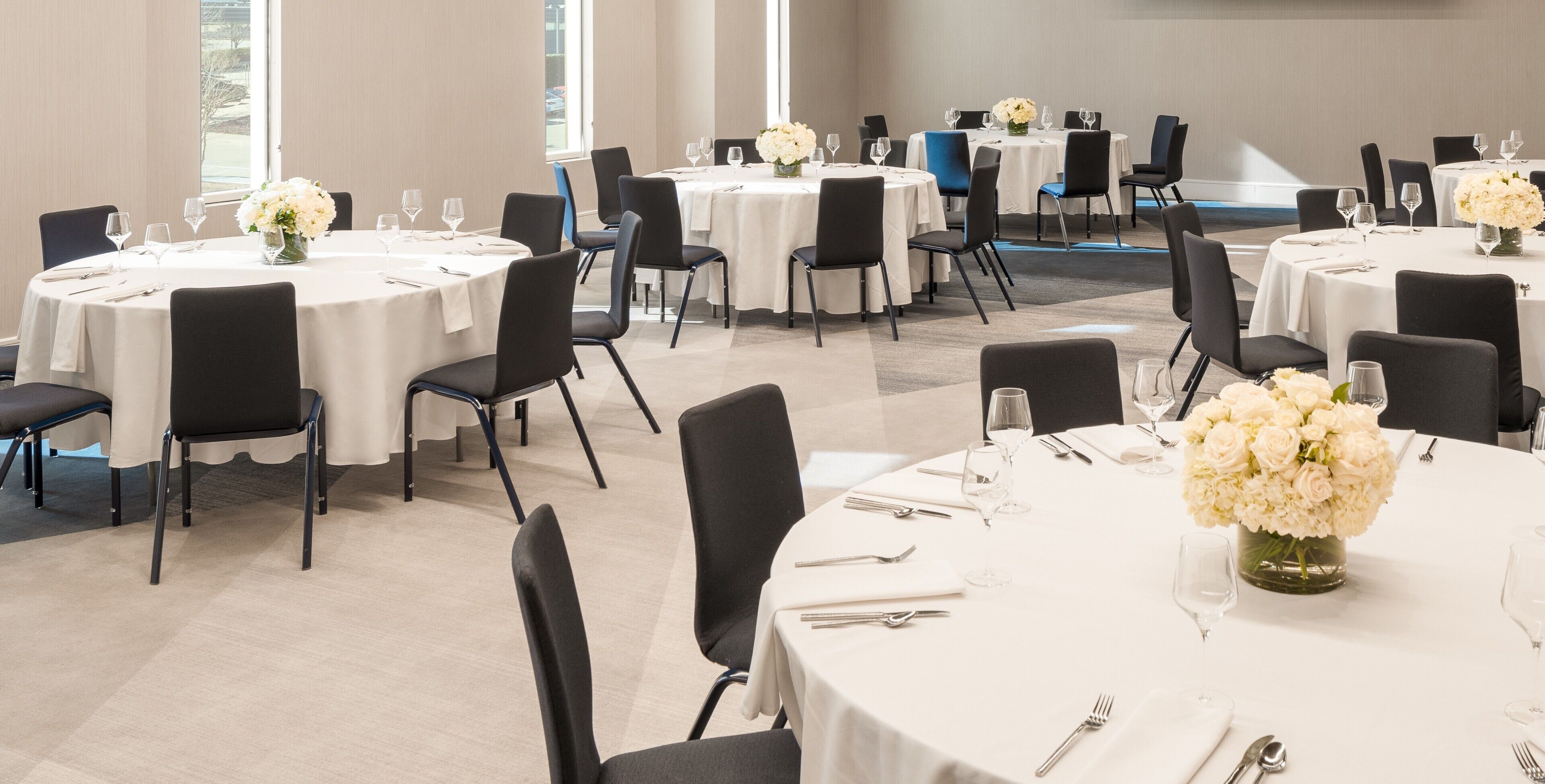 A conference room with round tables, black chairs, and white tablecloths.