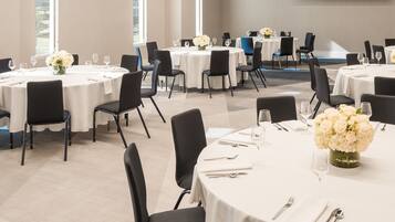 A conference room with round tables, black chairs, and white tablecloths.
