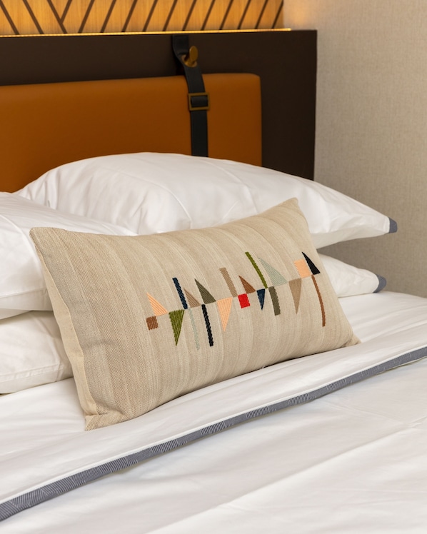 A bed with white linens, a beige pillow with a geometric pattern, and a brown headboard.
