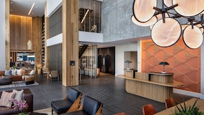 A spacious lobby with a reception desk, seating areas, and a staircase leading to upper floors. - The Ellison, Oklahoma City, a Tribute Portfolio Hotel (Oklahoma City)