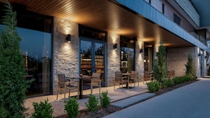 A modern building with a covered outdoor seating area, stone pillars, and glass doors. - The Ellison, Oklahoma City, a Tribute Portfolio Hotel (Oklahoma City)