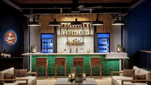 Uma área de bar com balcão, prateleiras cheias de garrafas e assentos com uma mesa em primeiro plano.