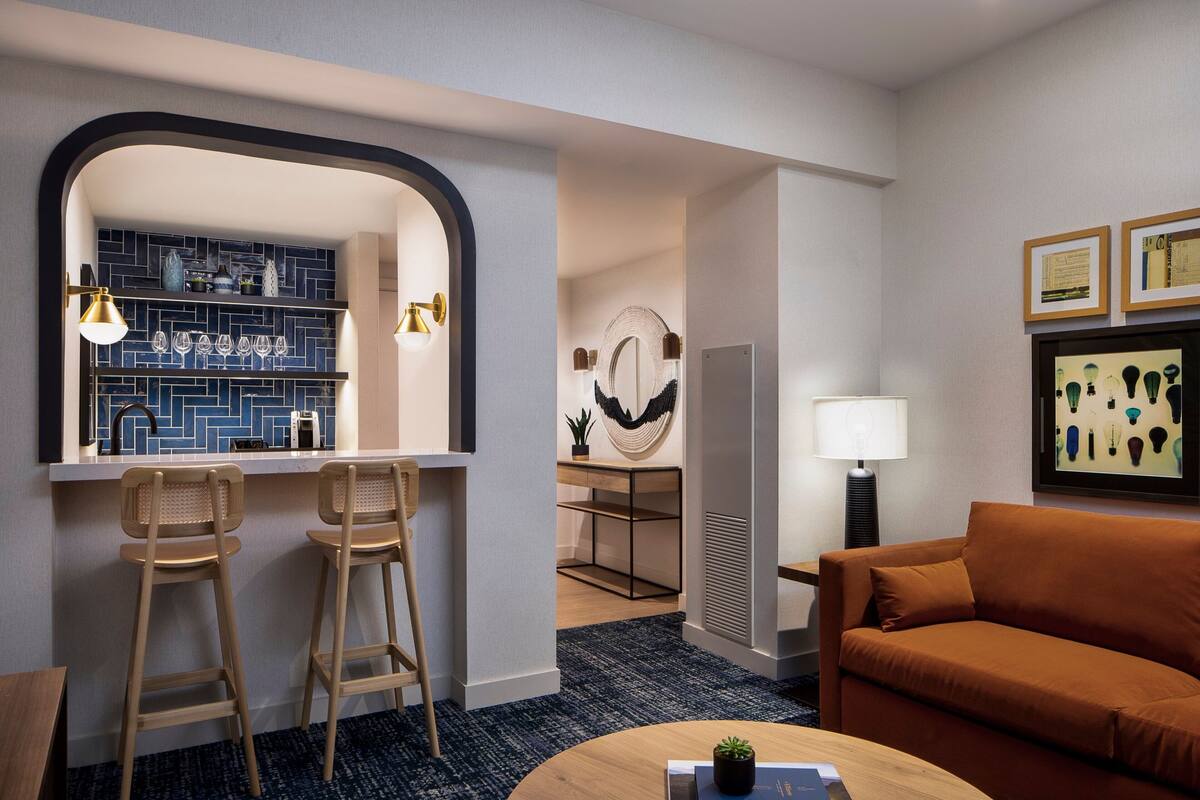 A modern hotel room with a bar area, a sofa, and a coffee table.