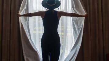 Una persona in piedi in una stanza con una grande finestra e tende.