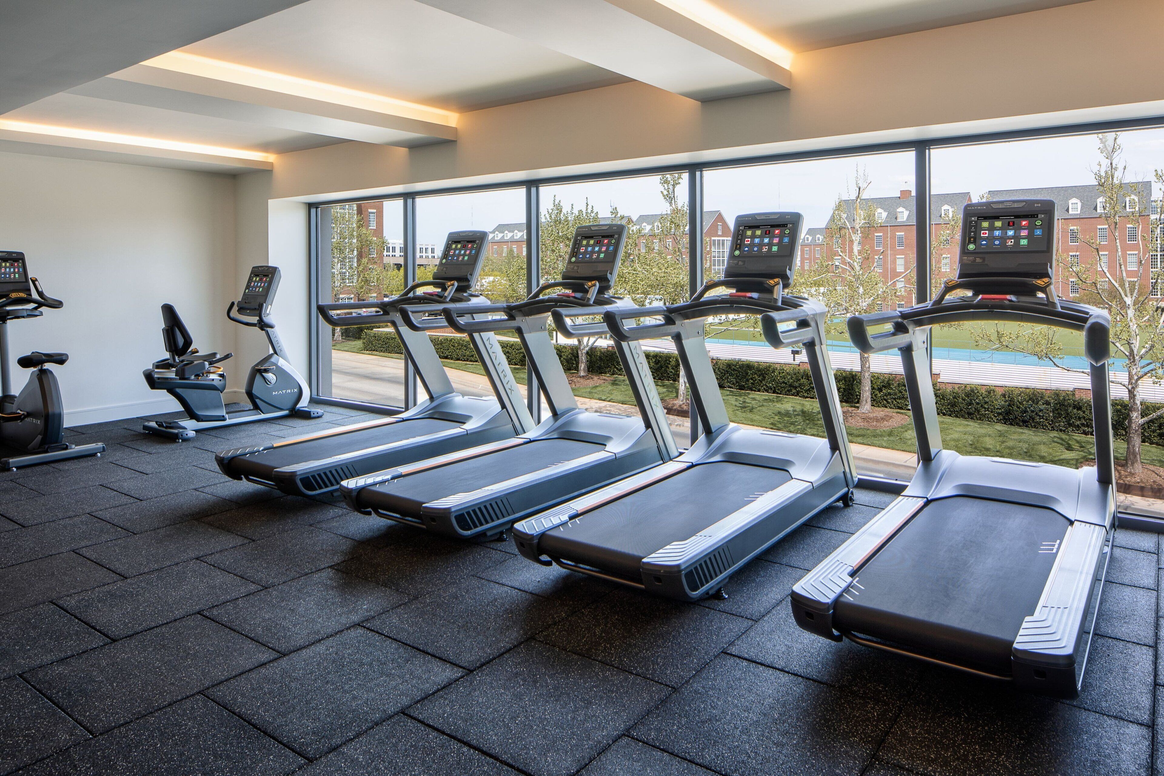 Ein Fitnessstudio mit Reihe von Laufbändern, großen Fenstern und Blick auf Gebäude.