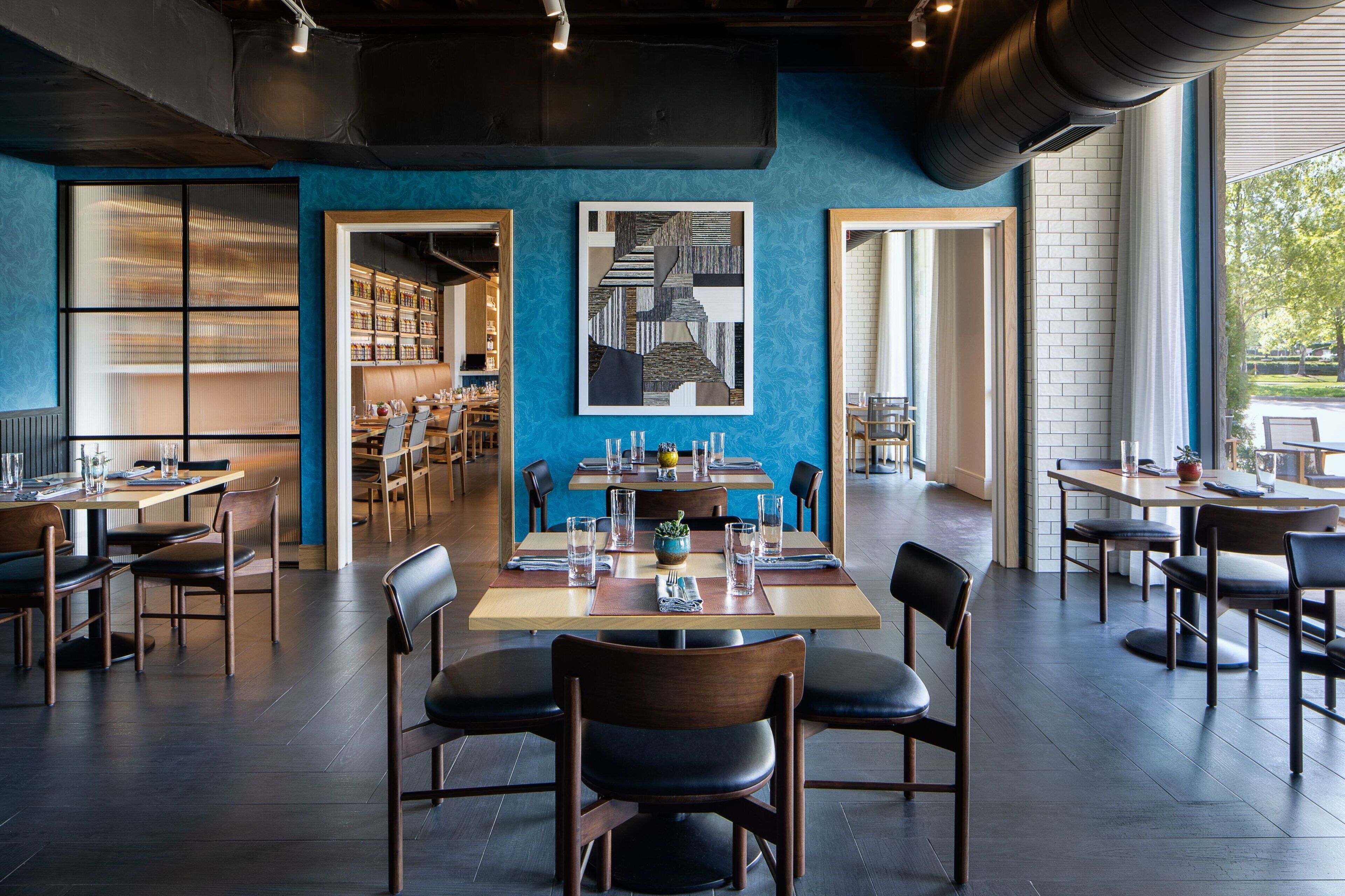 A restaurant with a modern interior, featuring wooden tables and chairs, a blue accent wall, and artwork on the wall.