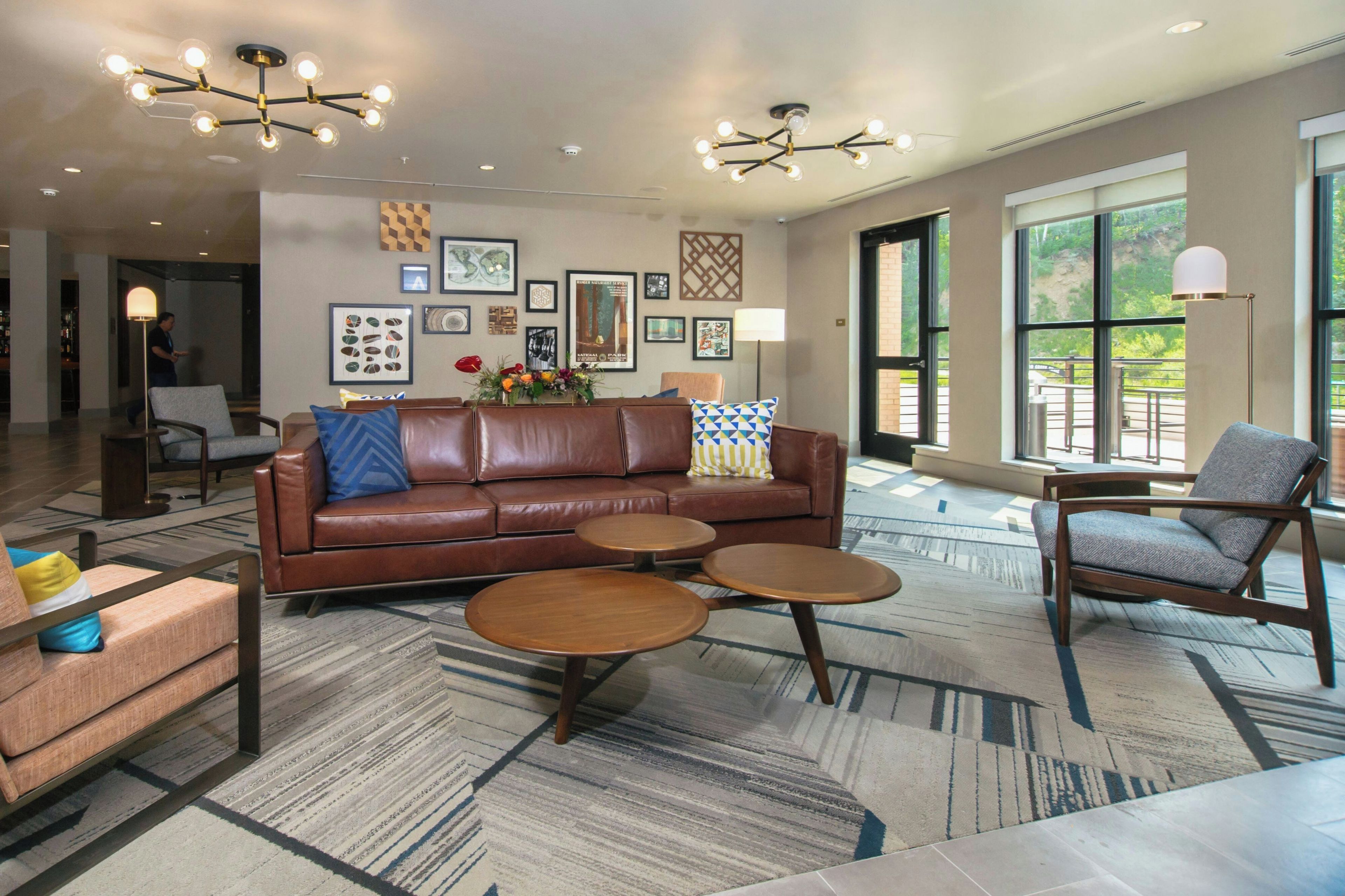A modern living room with a brown leather sofa, two round wooden side tables, and a grey armchair.