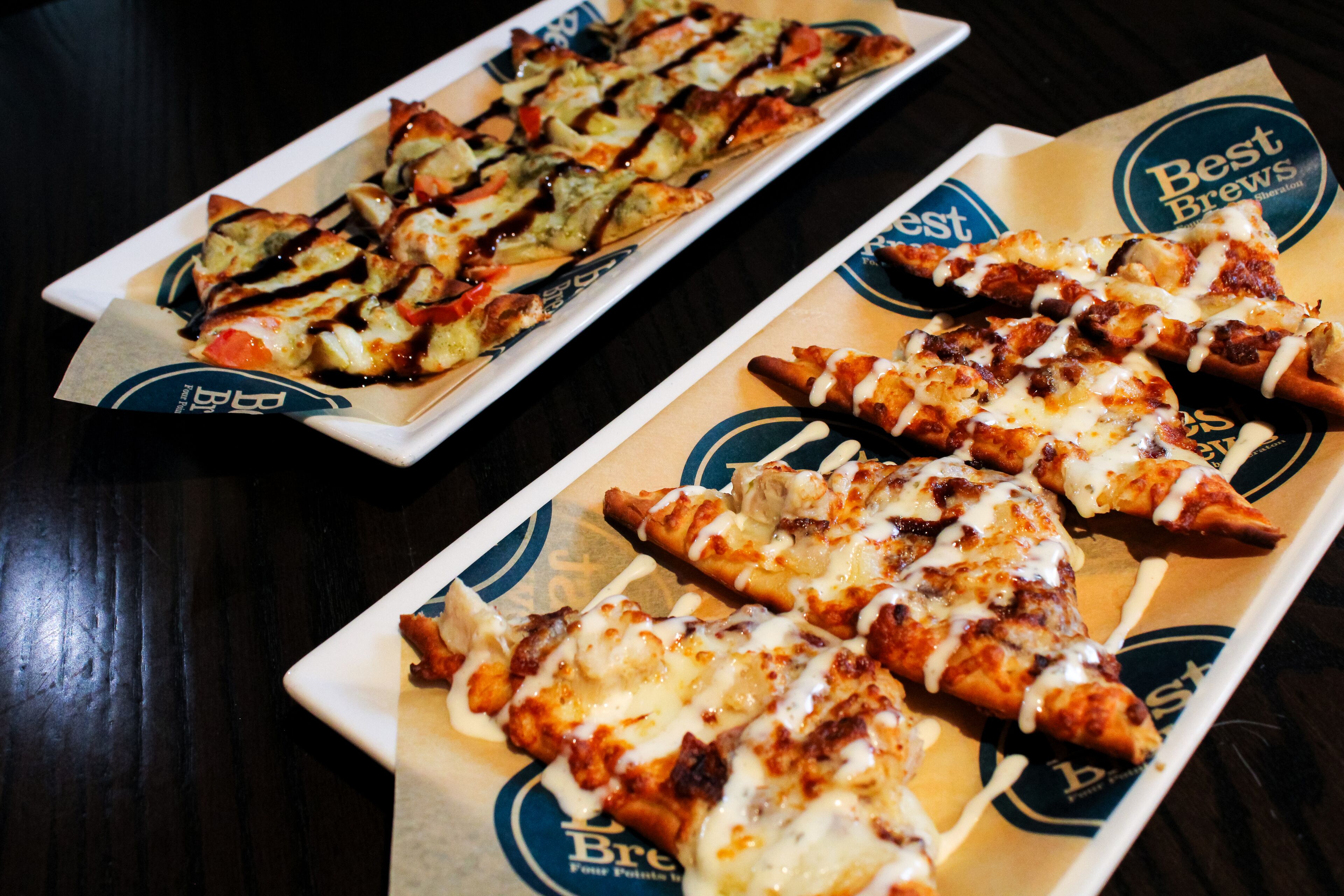 Two rectangular plates of pizza with toppings and a logo on the table.