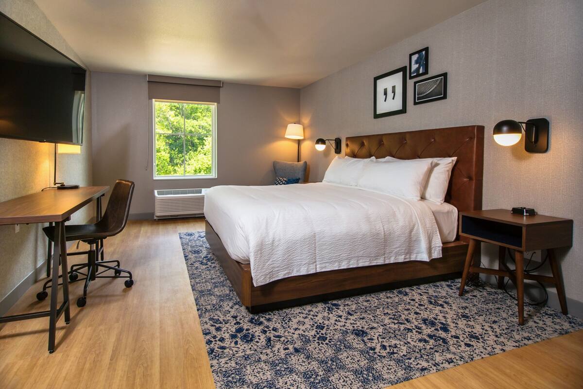 Une chambre d’hôtel équipée d’un lit, d’un bureau, d’une chaise et d’une fenêtre donnant sur un paysage verdoyant.