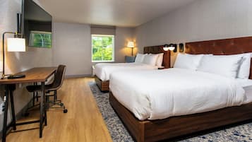 Une chambre d’hôtel avec deux lits, un bureau, une chaise, une grande fenêtre et un téléviseur à écran plat.