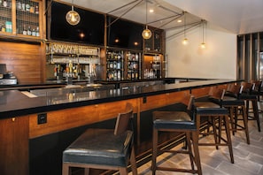 Uma área de bar com balcão longo, banquetas e diversos tipos de garrafas e copos.