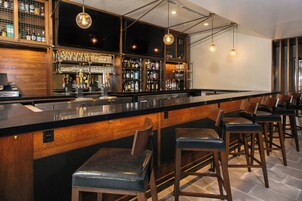 Una zona de bar con una barra larga, taburetes y una variedad de botellas y vasos.