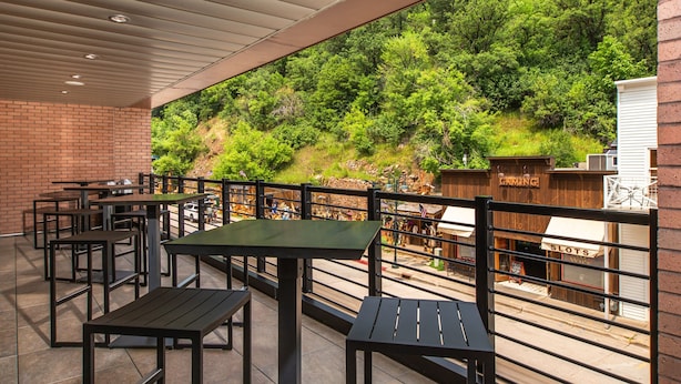 An outdoor patio with tables and chairs, a brick wall, and a view of a wooded hillside.