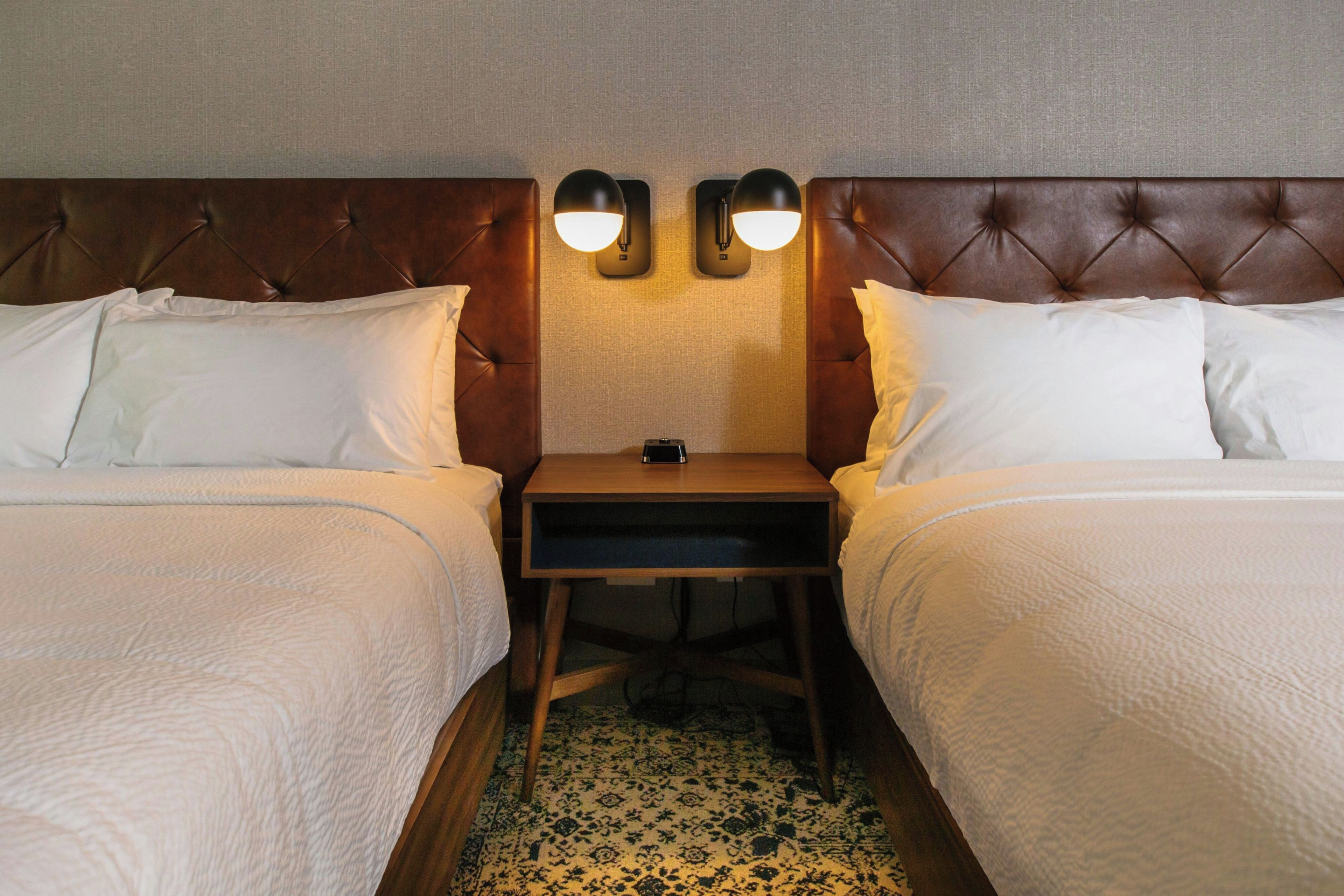 Ein Hotelzimmer mit zwei Betten, einem Nachttisch und zwei Wandlampen.