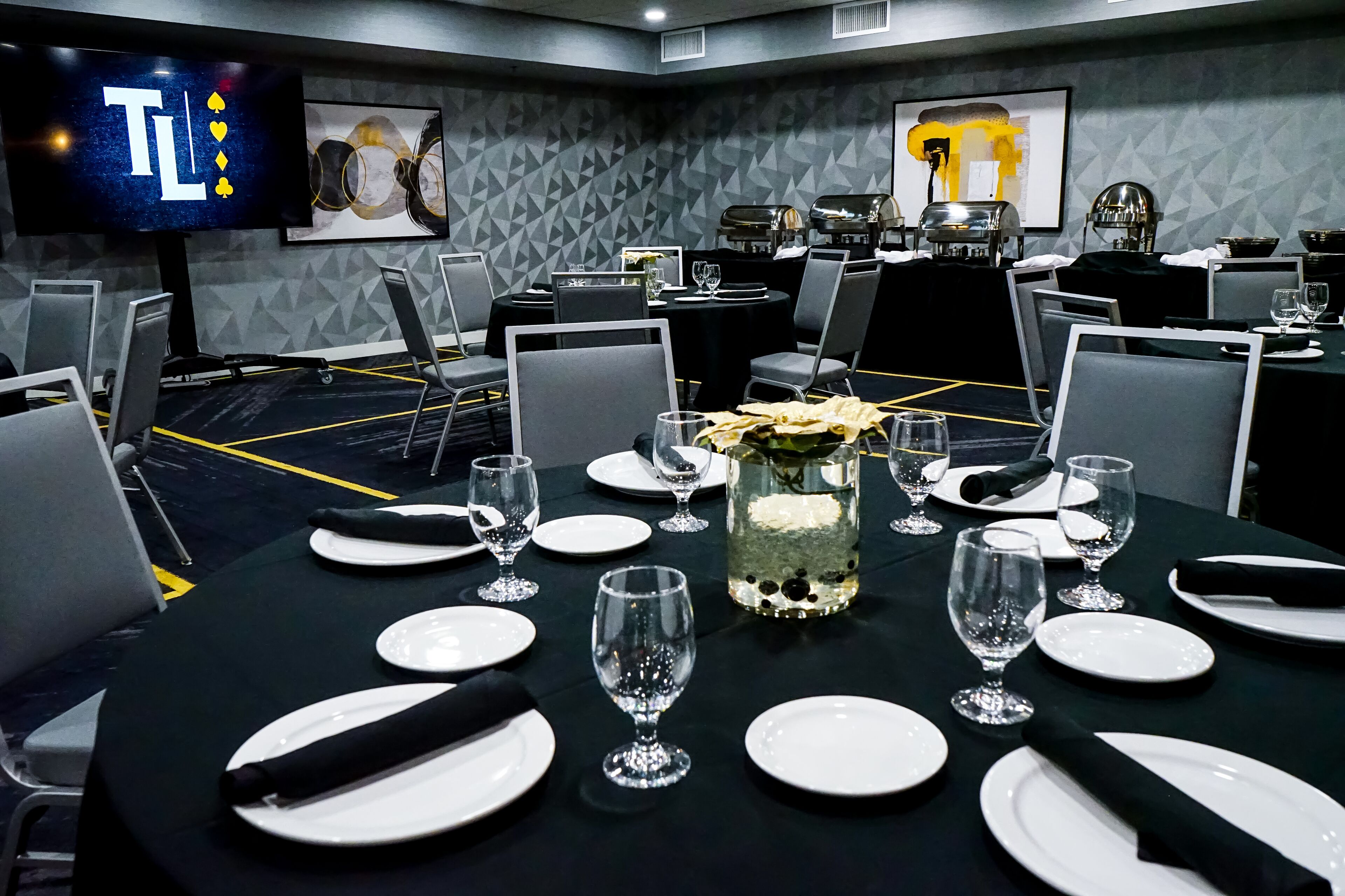 Un salón de conferencias con mesas dispuestas para una reunión, equipado con sillas, platos, vasos y un jarrón decorativo.