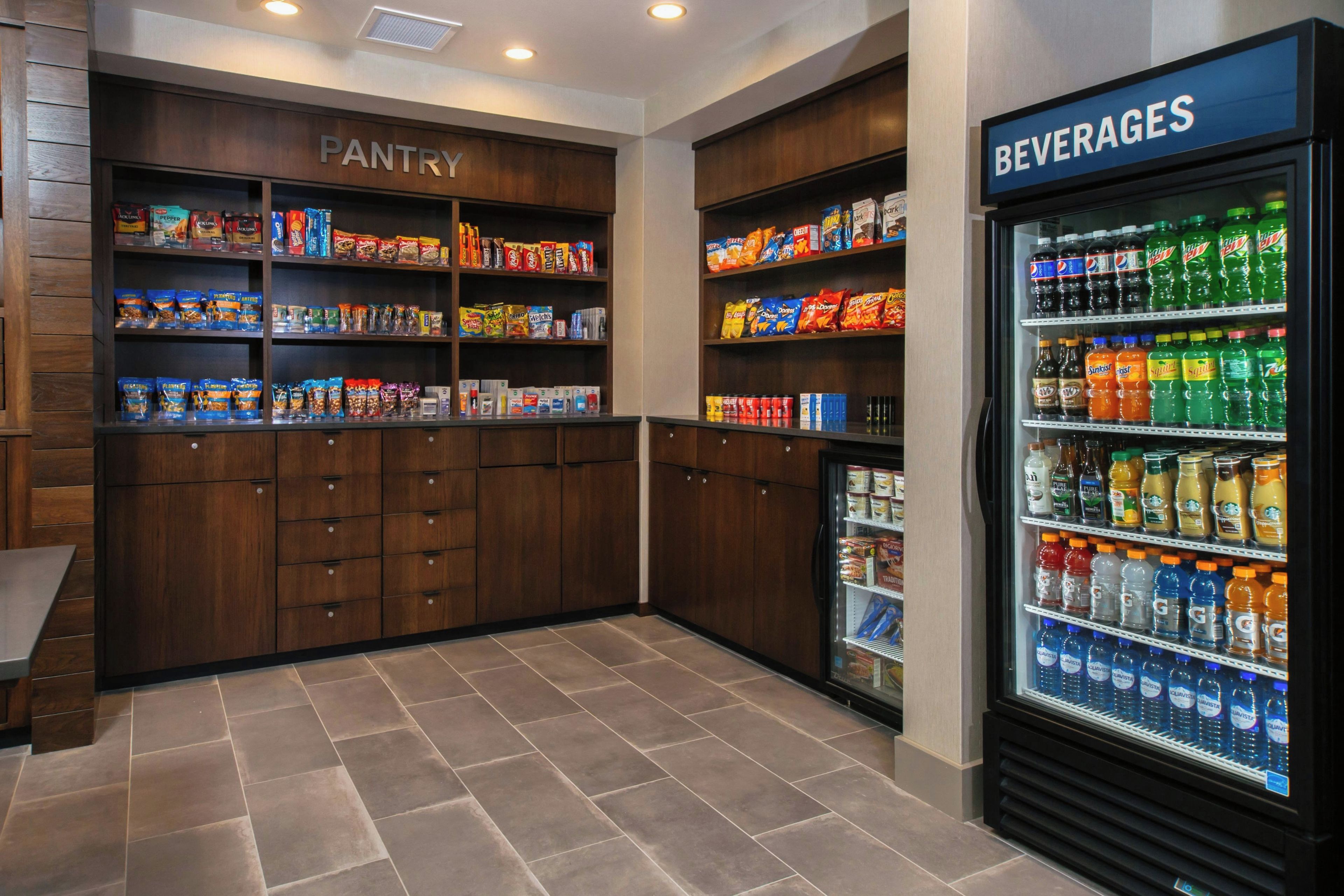 A hotel pantry and beverage refrigerator stocked with snacks and drinks.