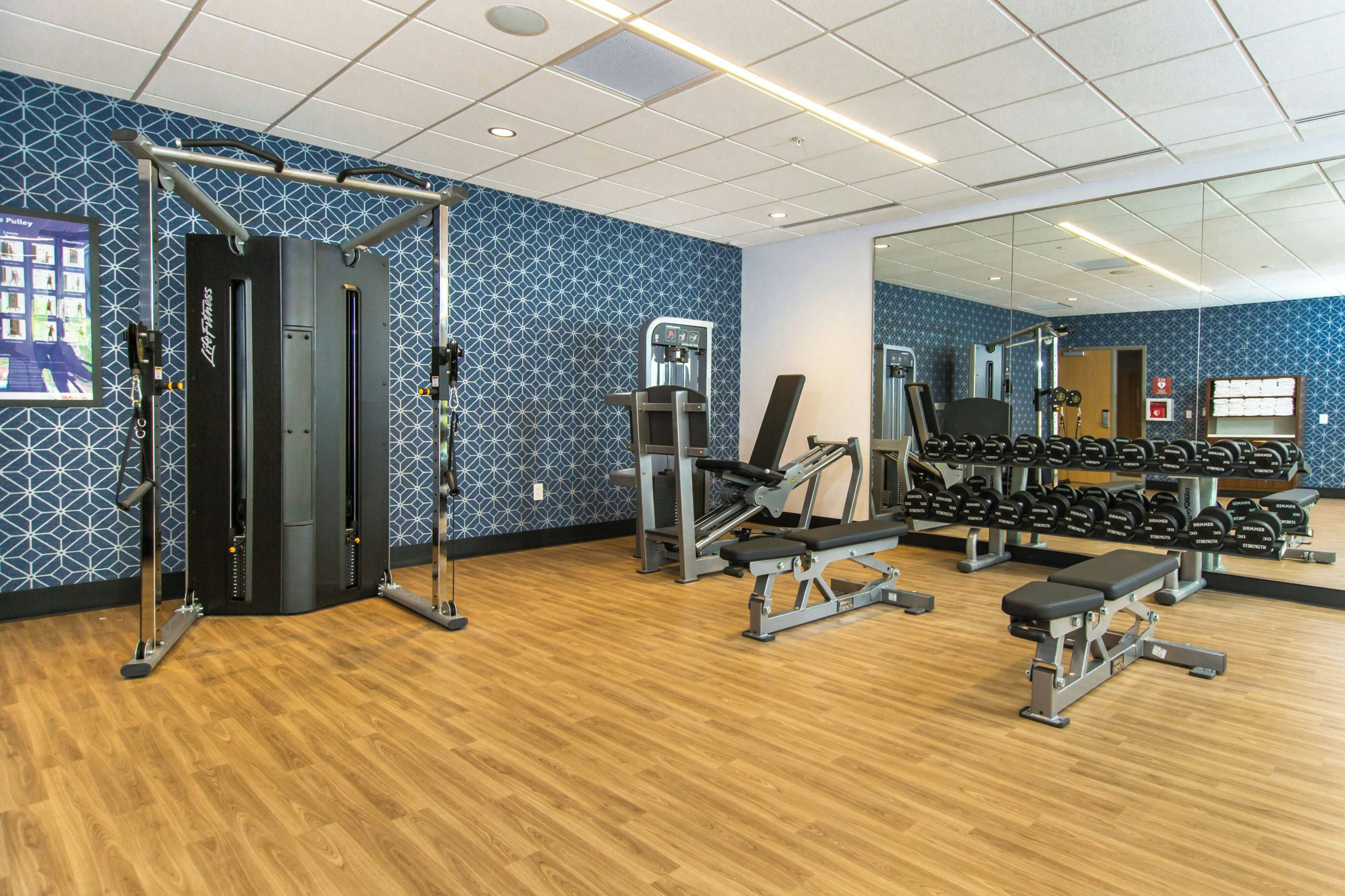 Une salle de sport équipée de matériel d’exercice, dotée d’un mur avec des miroirs et d’un autre mur décoré de motifs.