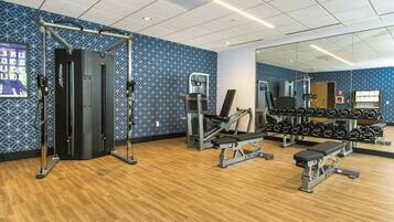 Une salle de sport équipée de matériel d’exercice, dotée d’un mur avec des miroirs et d’un autre mur décoré de motifs.
