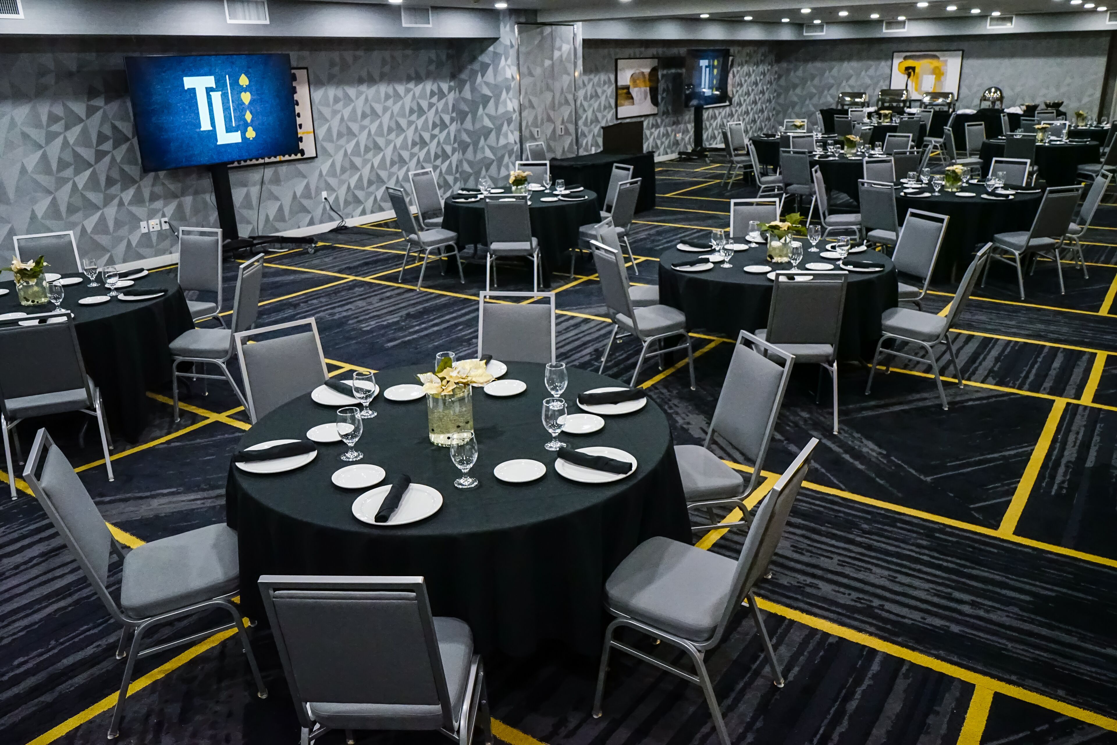Un salón de conferencias con varias mesas dispuestas para comer, equipado con sillas y una pantalla grande que muestra 'TL'.